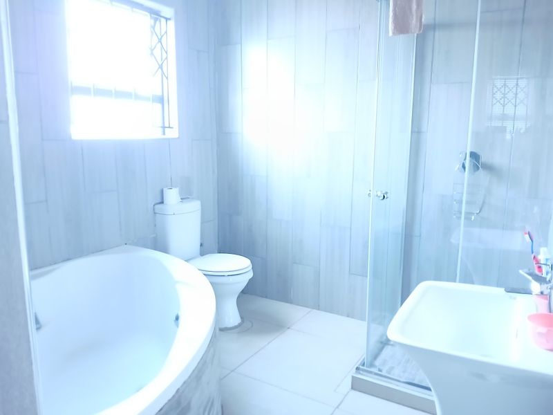 A bright, modern bathroom featuring a built-in bathtub, a separate glass-enclosed shower, a pedestal basin, and neutral wall and floor tiling.