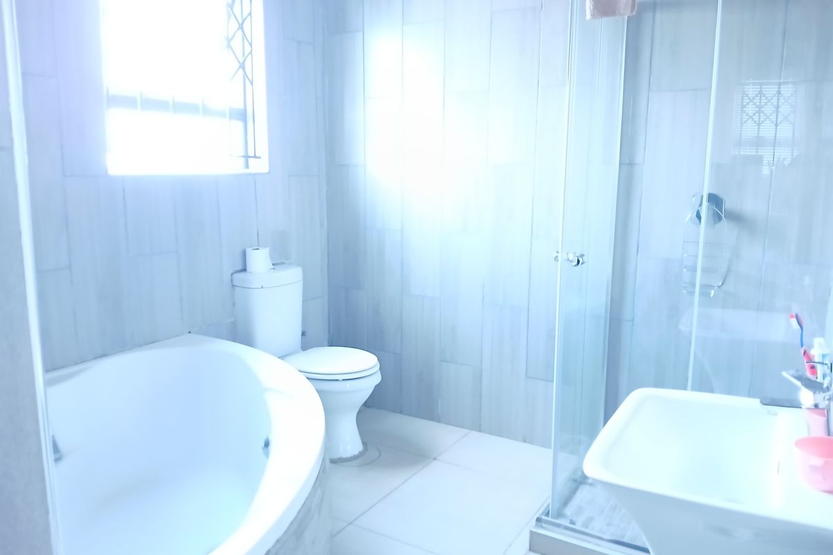 A bright, modern bathroom featuring a built-in bathtub, a separate glass-enclosed shower, a pedestal basin, and neutral wall and floor tiling.