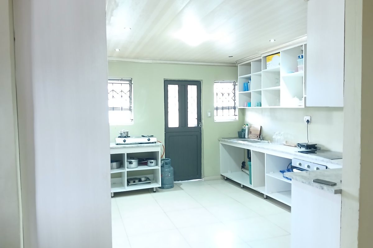 A functional kitchen space featuring open shelving, tiled flooring, and built-in cabinetry, with direct access to the exterior via a rear door.