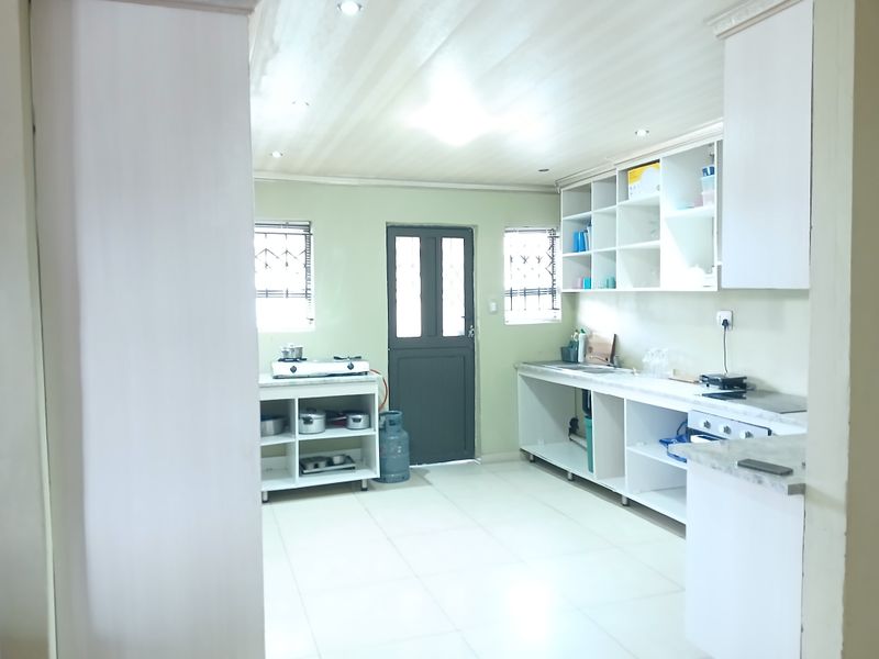 A functional kitchen space featuring open shelving, tiled flooring, and built-in cabinetry, with direct access to the exterior via a rear door.