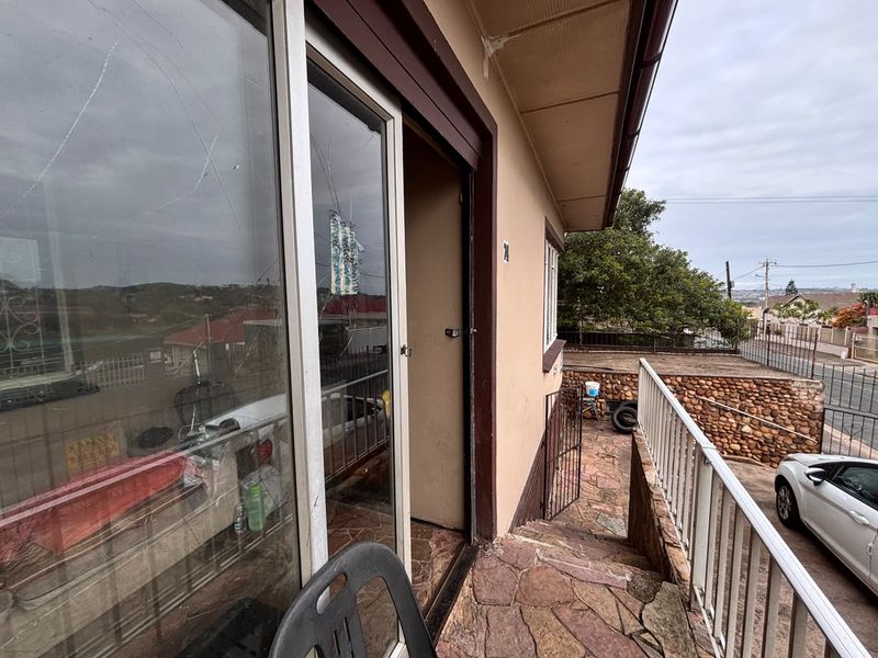 An exterior balcony area featuring stone paving and a metal railing, currently showing signs of wear and a cracked sliding glass door.