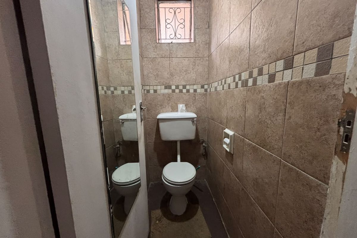 A compact guest bathroom featuring full-height ceramic wall tiling, a standard toilet, and a small window with a security gate.