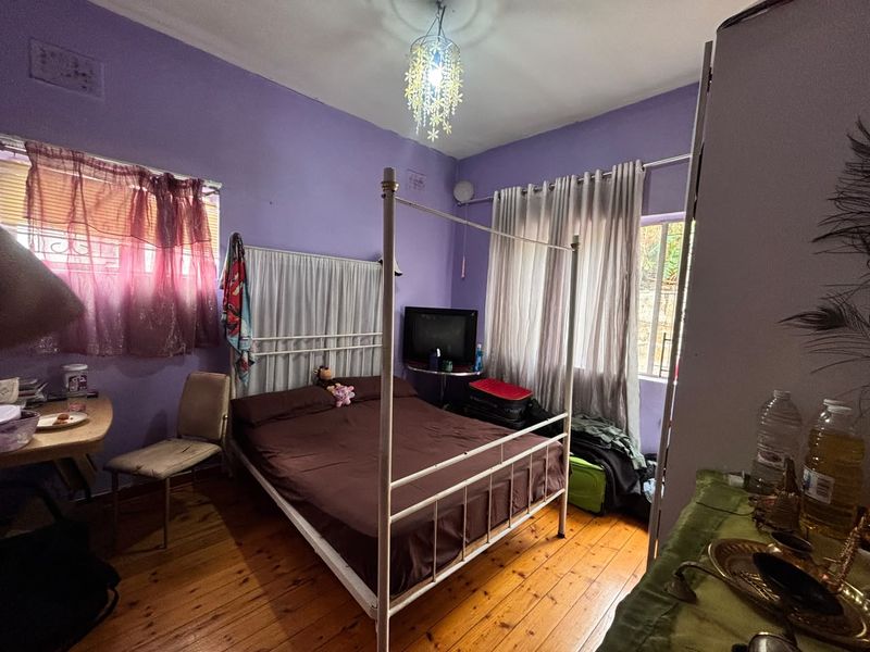 A bedroom featuring hardwood flooring, purple painted walls, and security bars on the windows, offering a functional space with potential for cosmetic updates.