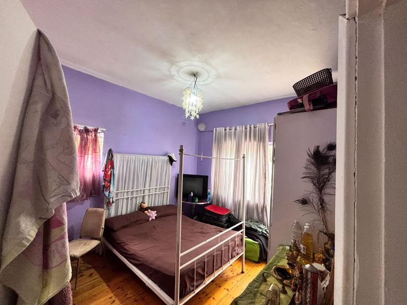 A bedroom featuring hardwood flooring and a central light fixture, currently requiring cosmetic updates to the walls and ceiling.