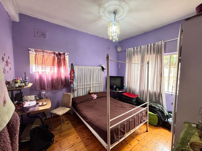 A bedroom featuring timber flooring, a decorative ceiling rose, and dual windows with curtain rods, currently finished in a vibrant purple wall color.