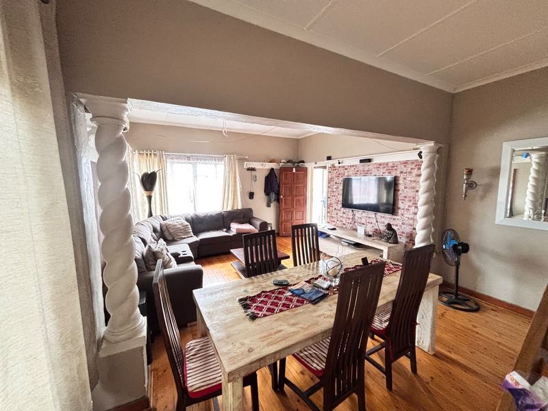 Open-plan living and dining area featuring hardwood floors, decorative spiral columns, and an exposed brick feature wall.