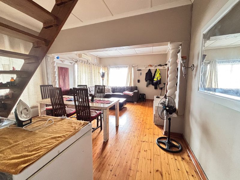 Open-plan living and dining area featuring polished timber flooring, a wooden staircase, and decorative columns, offering a versatile space for family living.
