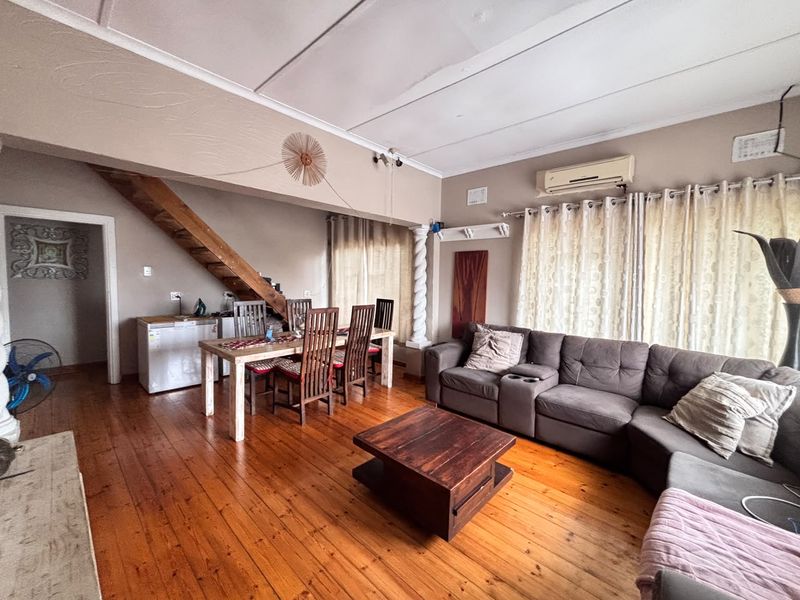 Open-plan living and dining area featuring polished wooden flooring, a staircase, and a wall-mounted air conditioning unit.
