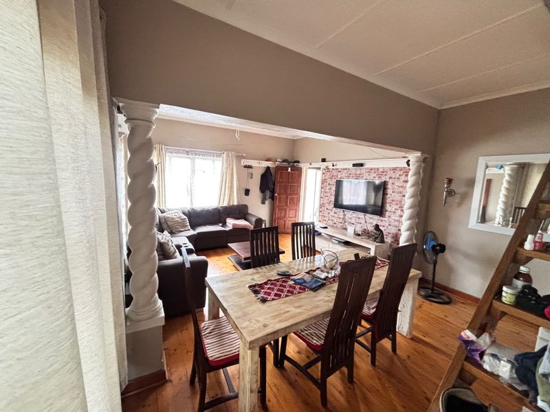 Open plan living and dining area featuring hardwood flooring, decorative spiral columns, and an exposed brick feature wall.