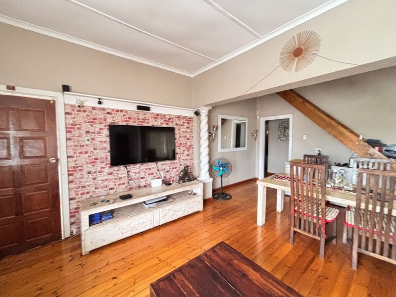 Open-plan living and dining area featuring polished hardwood flooring, a decorative brick-effect feature wall, and an exposed timber beam.