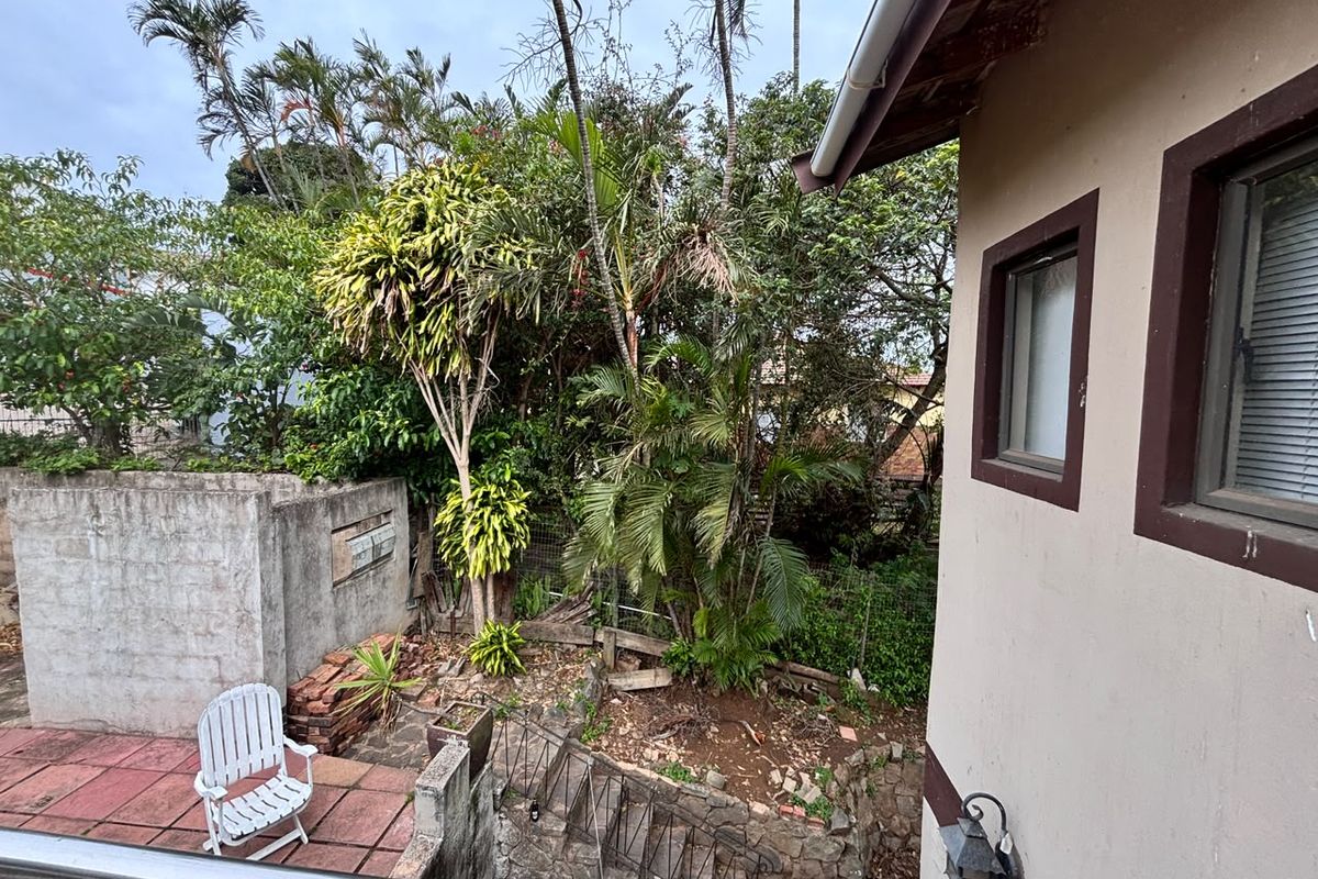 Rear exterior view showing a paved patio area, stone retaining wall, and established garden foliage adjacent to the house structure.