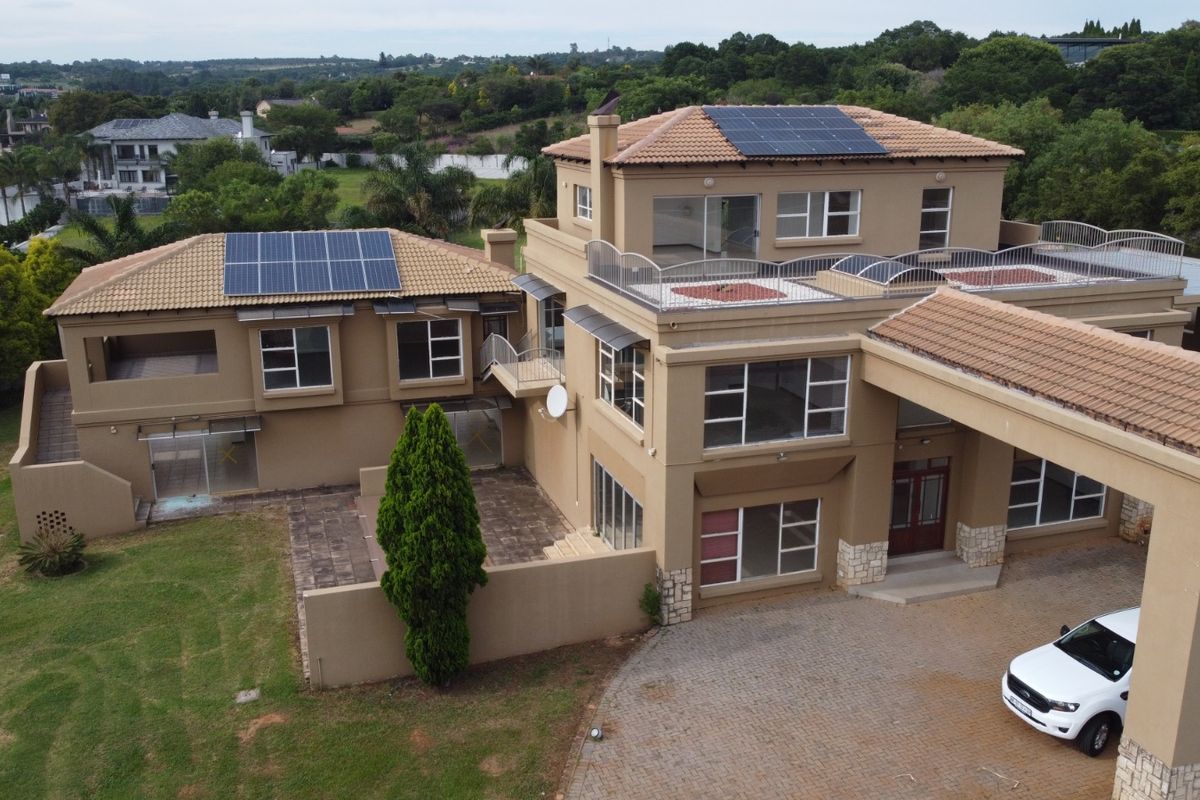 Aerial view of a multi-level residential property featuring solar panels, a tiled roof, paved driveway, and multiple balconies set within a landscaped estate.