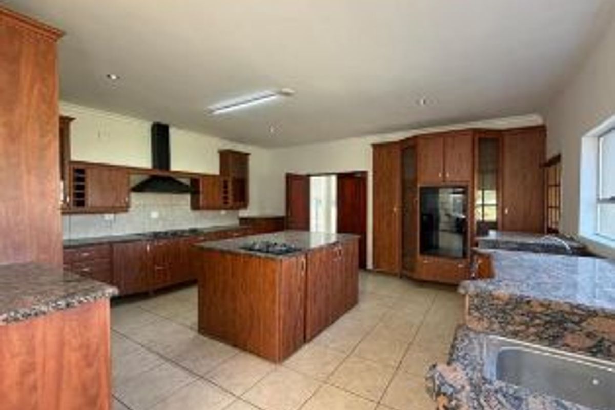 Spacious kitchen featuring extensive wooden cabinetry, granite countertops, a central island with a cooktop, and tiled flooring throughout.