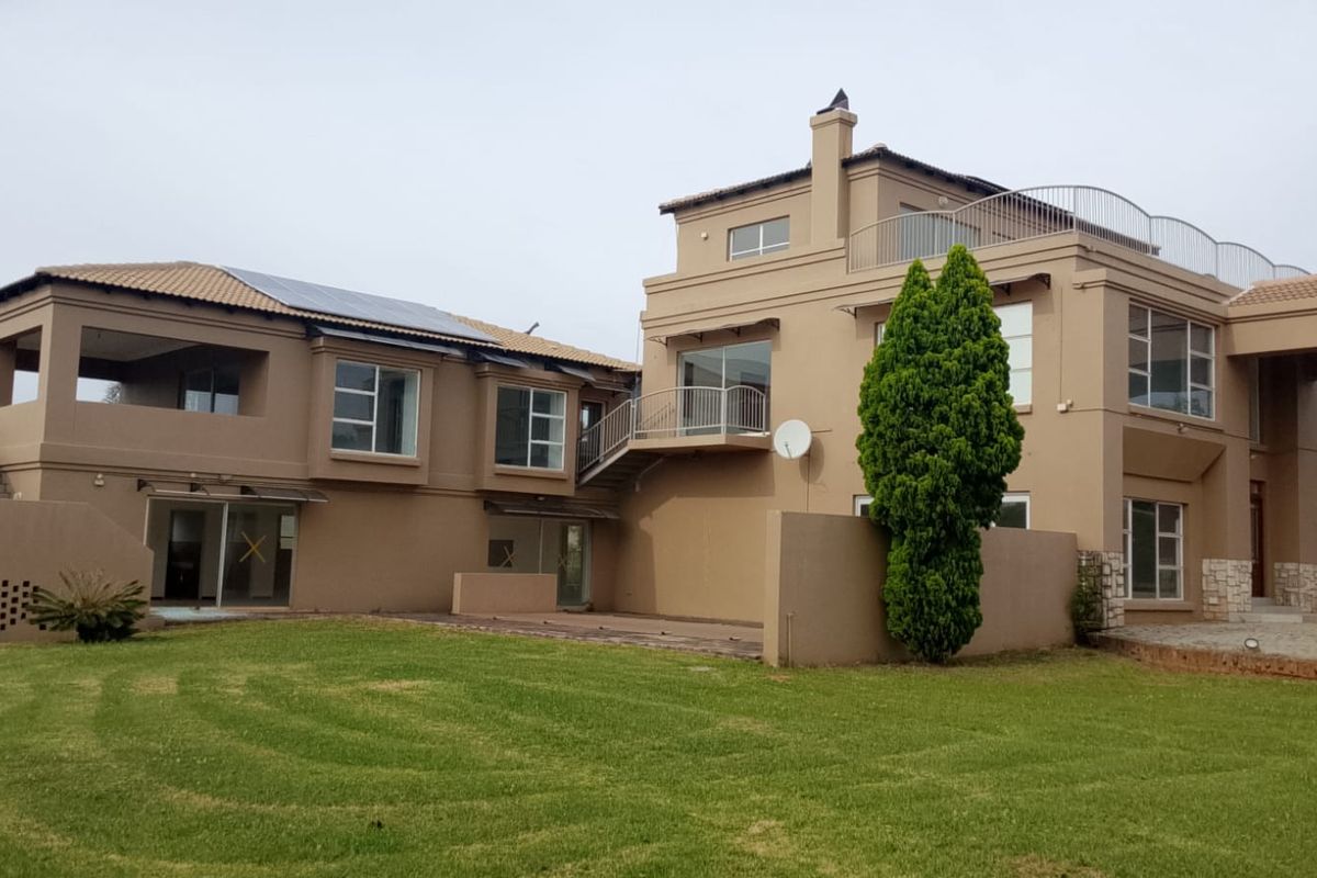 Rear view of a multi-story residential property featuring a large lawn, paved patio, balconies, and solar panels on the roof.