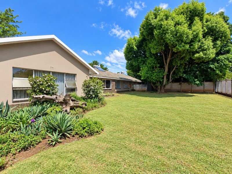 A spacious rear garden featuring a well-maintained lawn, mature trees, and a brick exterior facade with solar water heating panels on the roof.