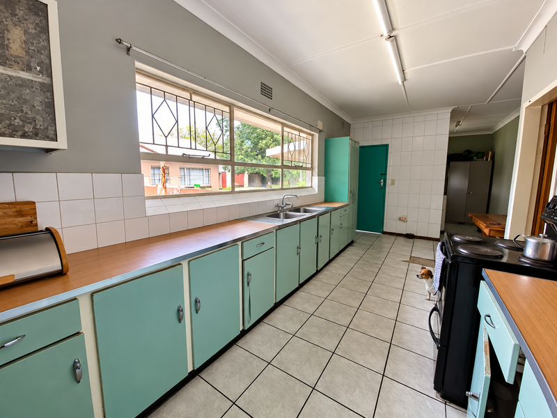 A functional kitchen featuring vintage-style cabinetry, laminate countertops, a double sink, and tiled flooring, offering significant potential for a modern renovation.