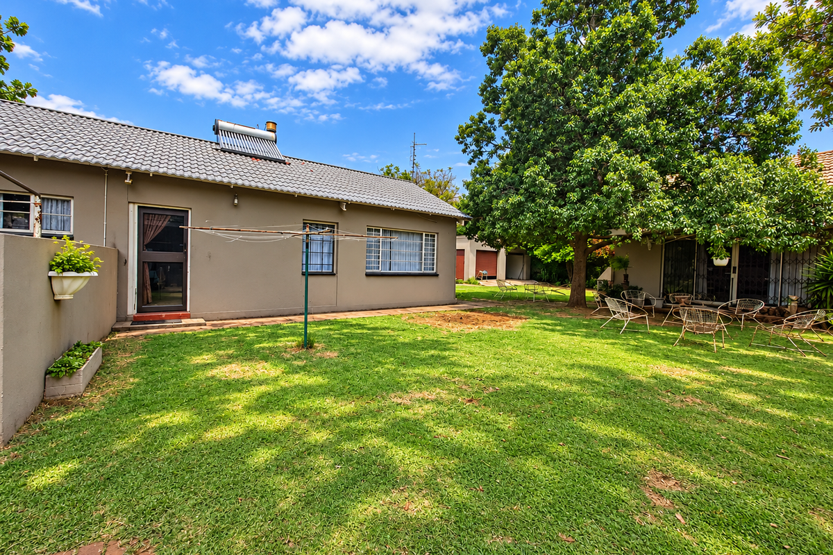 A spacious rear garden featuring a well-maintained lawn, brick paving, and a house exterior equipped with a solar water heating system.