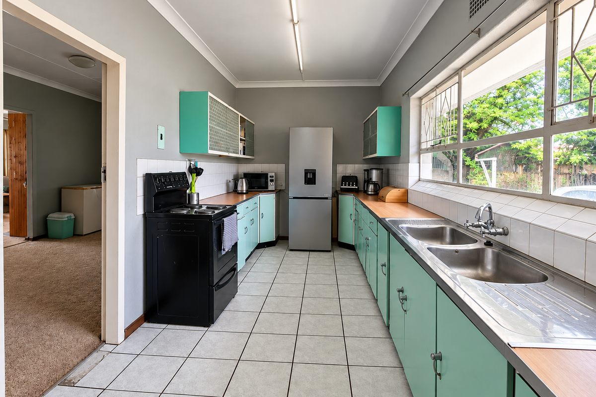 A functional kitchen featuring vintage-style cabinetry, a double stainless steel sink, tiled splashbacks, and a freestanding stove, with direct access to the adjacent living area.