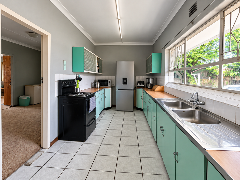 A functional kitchen featuring vintage-style cabinetry, a double stainless steel sink, tiled splashbacks, and a freestanding stove, with direct access to the adjacent living area.