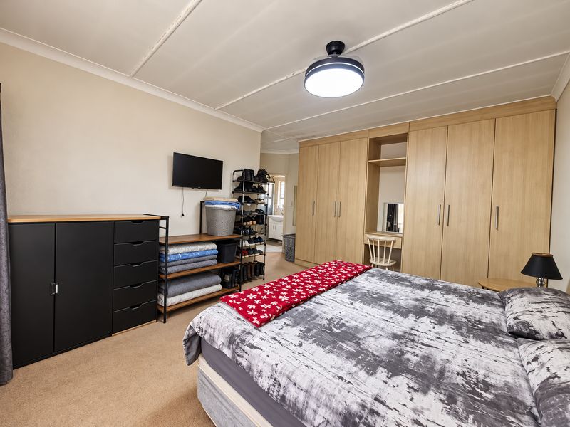 A spacious bedroom featuring extensive built-in wooden cupboards with an integrated vanity area, neutral wall finishes, and carpeted flooring.