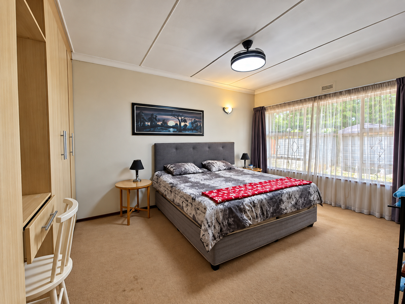 A well-maintained bedroom featuring built-in cupboards, a ceiling fan, and large windows with security gates, offering a comfortable and functional living space.