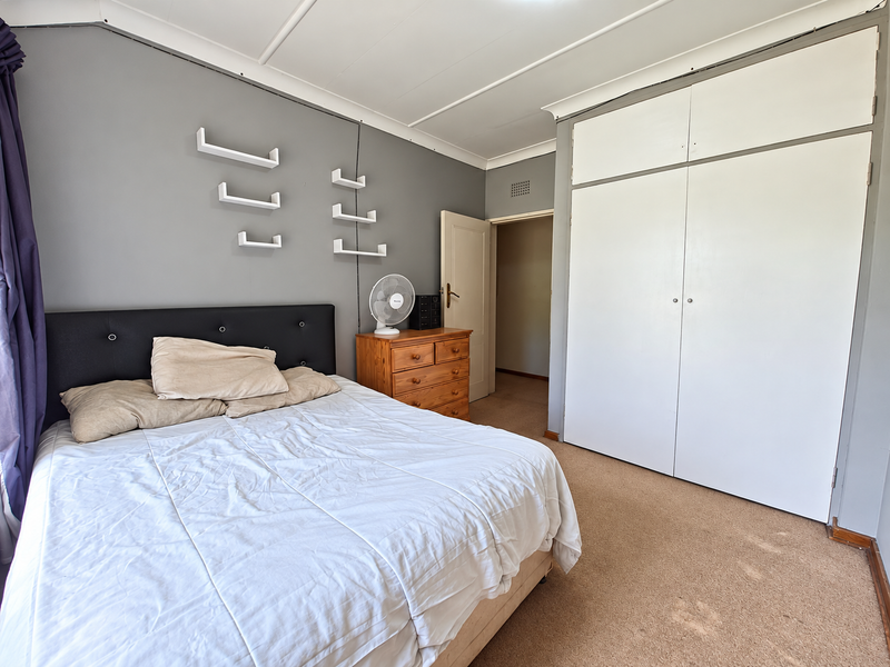 A bedroom featuring built-in wardrobes, carpeted flooring, and neutral grey wall tones, offering a functional space with potential for cosmetic updates.