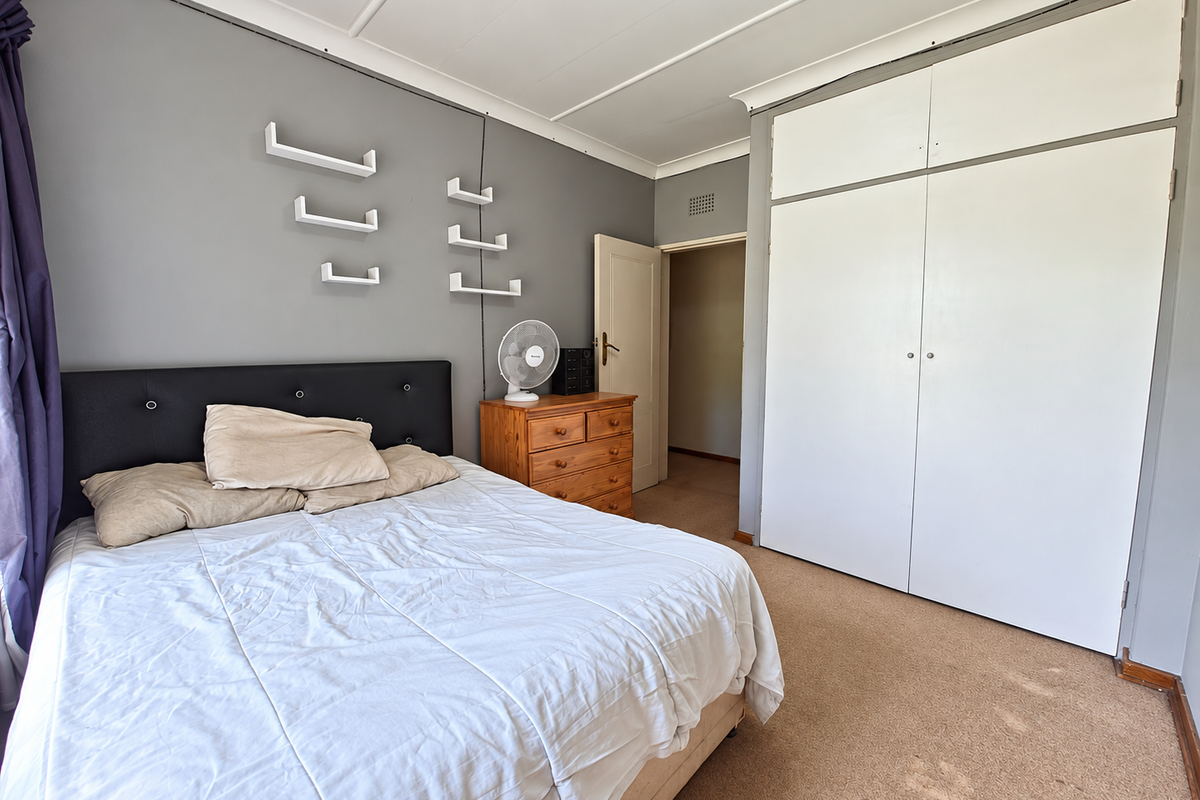 A bedroom featuring built-in wardrobes, carpeted flooring, and neutral grey wall tones, offering a functional space with potential for cosmetic updates.