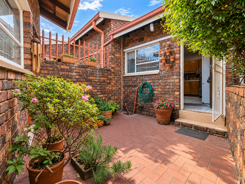 A private, enclosed brick-paved courtyard featuring face brick walls, secure gated access, and established garden elements, providing a low-maintenance outdoor living space.