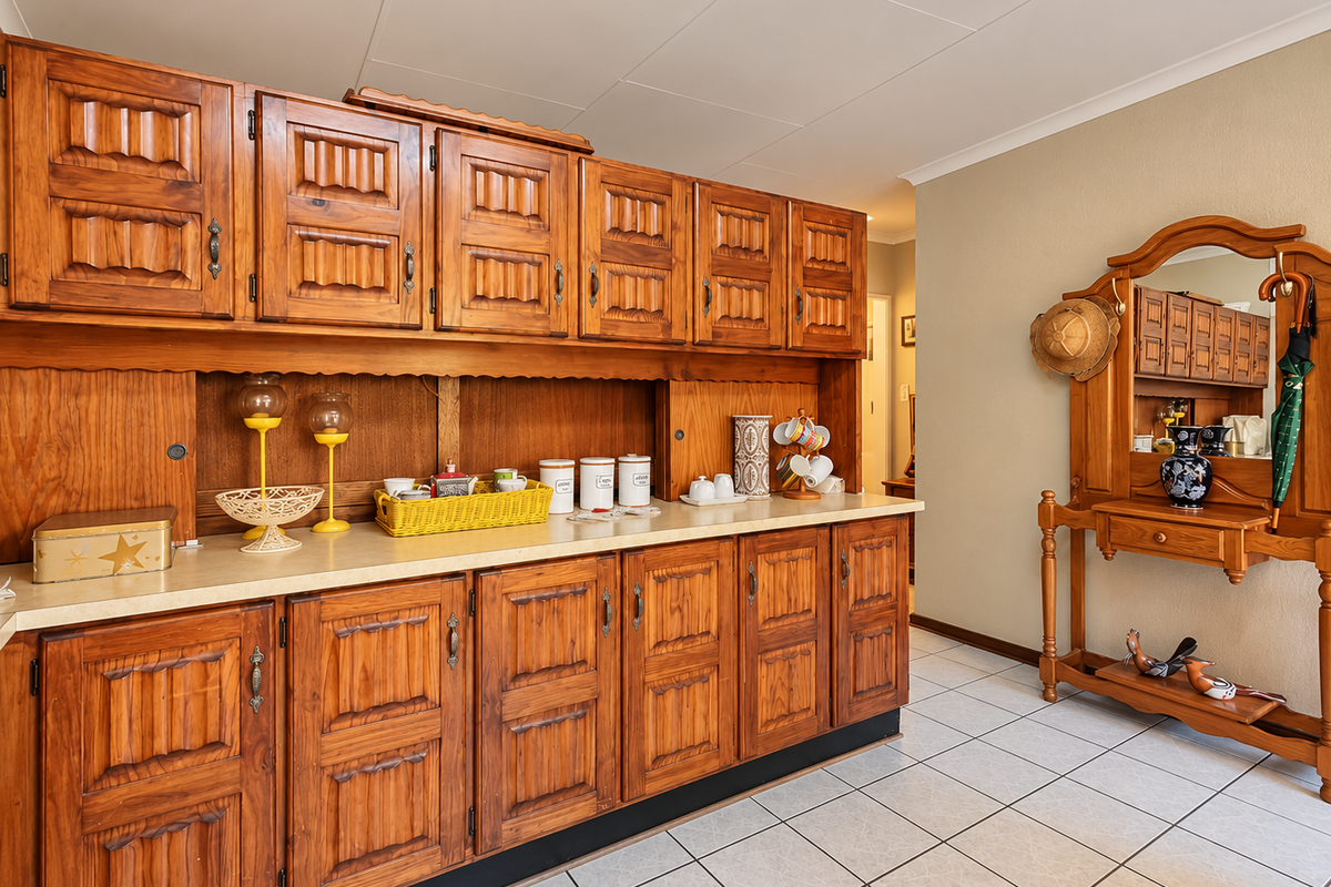 A kitchen area featuring extensive built-in wooden cabinetry, laminate countertops, and tiled flooring, offering ample storage space in a traditional style.