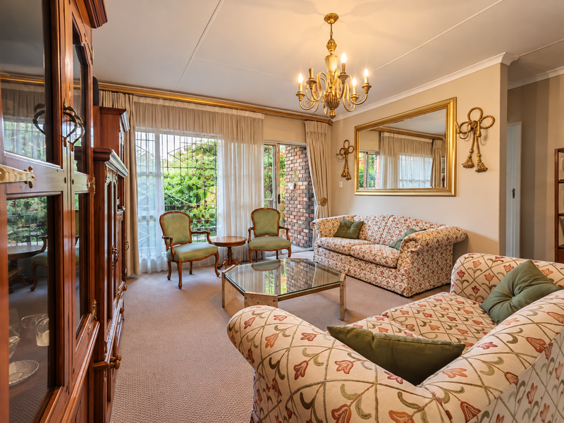 A well-maintained living room featuring a classic chandelier, wall-to-wall carpeting, and direct access to an outdoor patio area through sliding glass doors.
