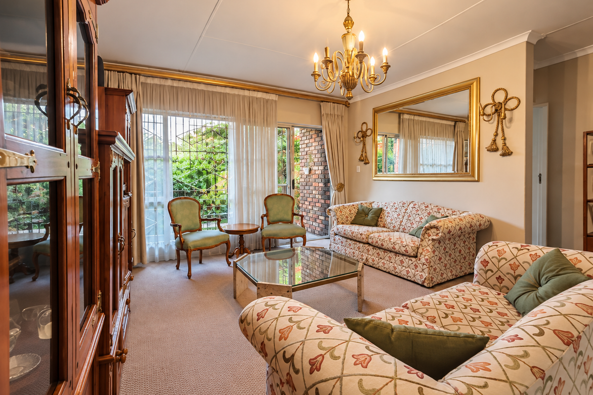 A well-maintained living room featuring a classic chandelier, wall-to-wall carpeting, and direct access to an outdoor patio area through sliding glass doors.