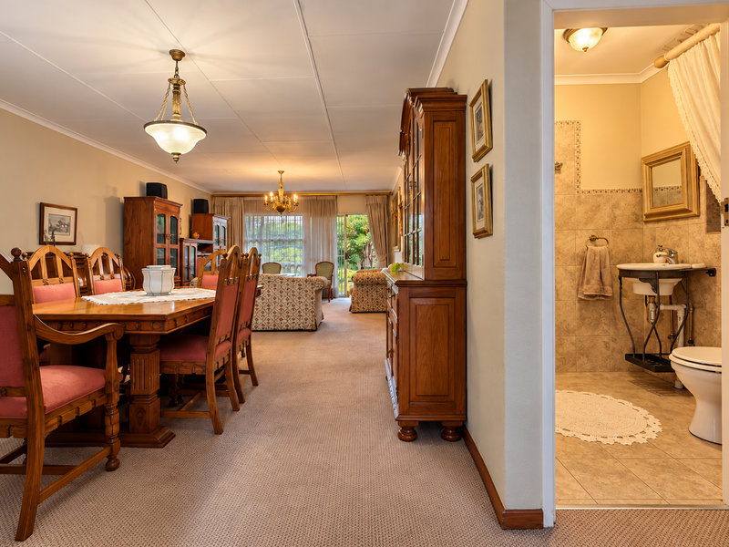Open-plan living and dining area featuring neutral carpeting, leading to a tiled bathroom with a pedestal basin and wall-mounted toilet.