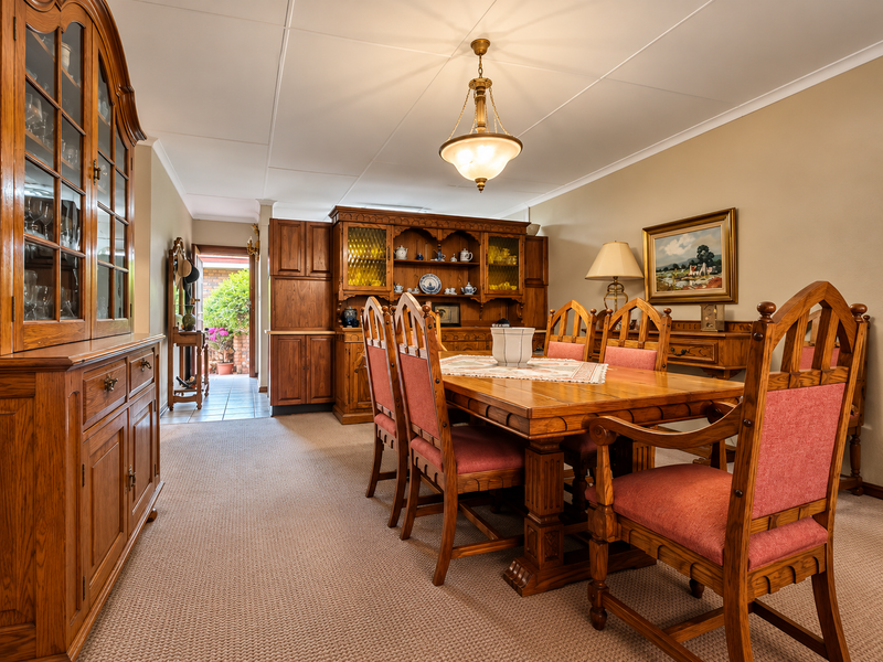 A traditional dining room featuring built-in wooden cabinetry, a central pendant light, and carpeted flooring, with an open transition to a tiled hallway.