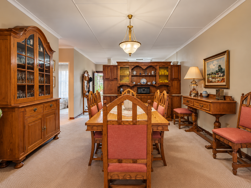 A traditional dining room featuring fitted wooden cabinetry, a central pendant light, and carpeted flooring, offering a classic and formal dining space.
