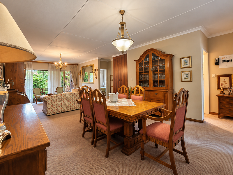 Spacious open-plan dining and living area featuring neutral carpeting, classic pendant lighting, and sliding glass doors leading to an outdoor patio space.