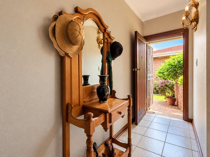 A bright entrance hall featuring tiled flooring and a security gate leading to an outdoor patio area.