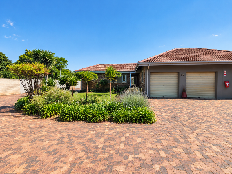 Front view of a retirement village residence featuring a double garage, paved driveway, and well-maintained landscaped garden.