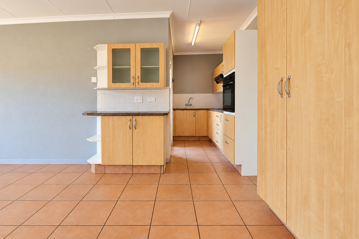 A clean, empty kitchen featuring light wood-look cabinetry, built-in oven, extractor fan, and tiled flooring, offering a functional layout ready for personalization.