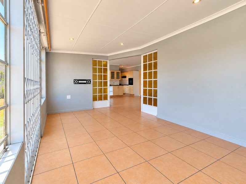 Spacious open-plan living area featuring neutral walls, tiled flooring, and recessed lighting, with a clear view through to the adjoining kitchen.