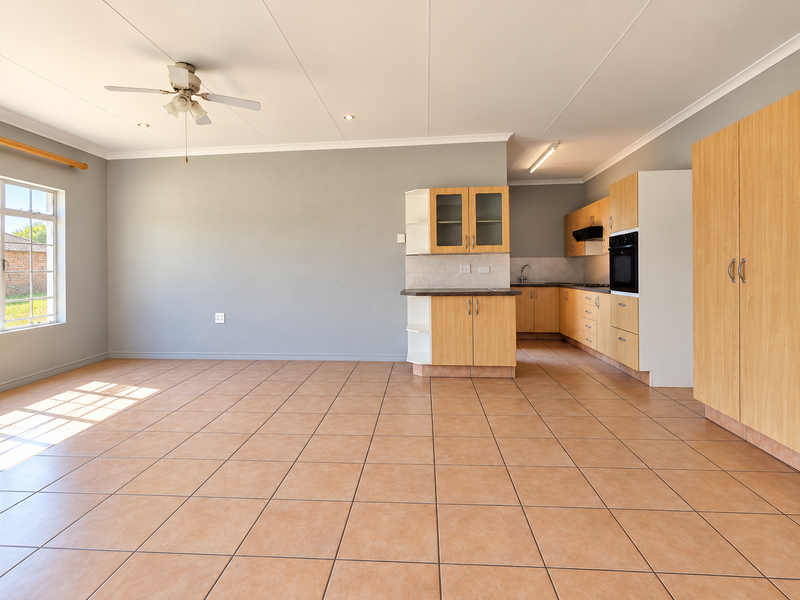 Spacious open-plan living and kitchen area featuring light wood cabinetry, built-in oven, tiled flooring, and a ceiling fan in a neutral setting.