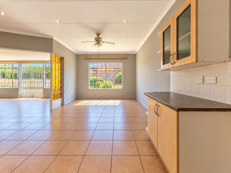 Spacious open-plan living area featuring neutral tiled flooring, recessed lighting, a ceiling fan, and a functional kitchen corner with built-in cabinetry.