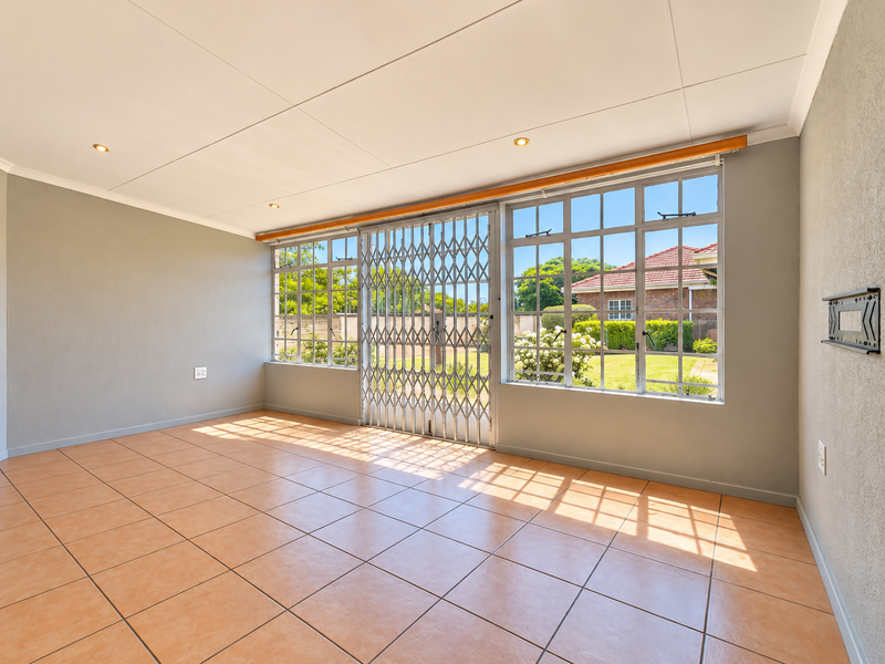 A bright and spacious living area featuring neutral walls, tiled flooring, recessed lighting, and a secure sliding door leading to the garden.