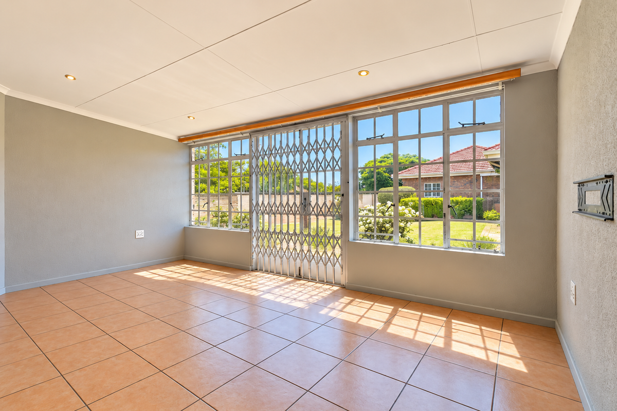 A bright and spacious living area featuring neutral walls, tiled flooring, recessed lighting, and a secure sliding door leading to the garden.