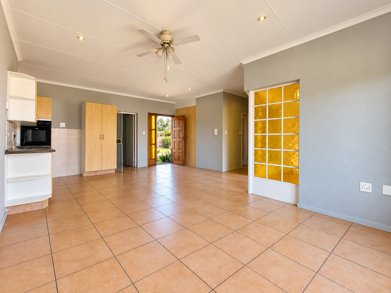 Spacious open-plan living area featuring tiled floors, a ceiling fan, built-in kitchen cabinetry with oven, and a distinctive decorative glass room divider.