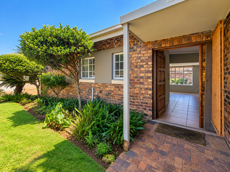 A well-maintained retirement village home featuring a classic brick facade, landscaped garden, and a welcoming paved entrance leading into an open-plan interior.