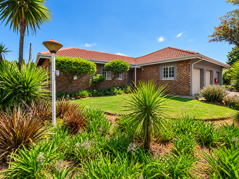 A well-maintained retirement village home featuring a face brick facade, tiled roof, double garage, and established landscaped garden.