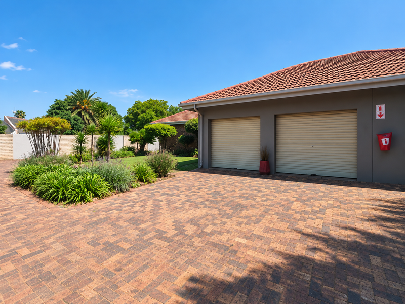 Well-maintained front exterior featuring a double garage with roller doors, a paved driveway, and a neatly landscaped garden area.