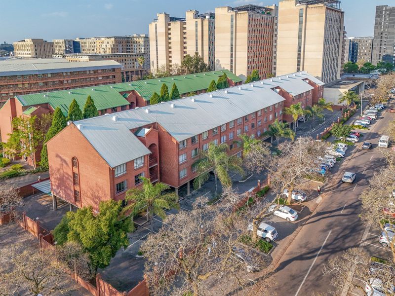 Aerial view of a multi-story brick apartment complex featuring a metal roof, surrounding landscaped grounds, and dedicated paved parking areas.