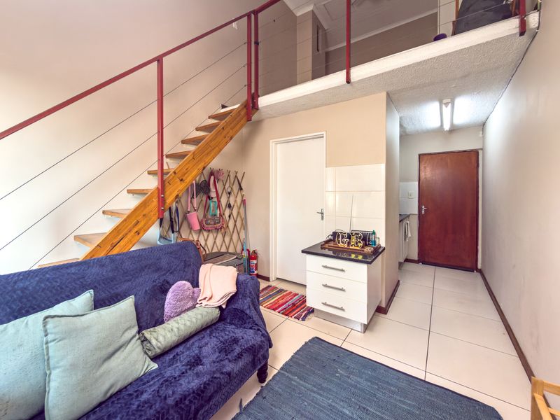 Open plan living area featuring a mezzanine level, staircase, and tiled flooring, providing a functional layout with access to a kitchenette and additional rooms.