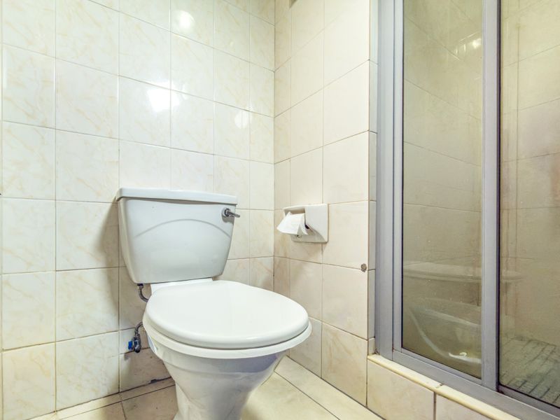 A compact bathroom featuring a standard toilet and a glass-enclosed shower, finished with dated ceramic wall tiles.